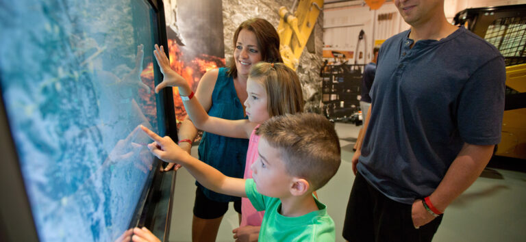 A family of four using a touchscreen at the Caterpillar Visitors Center