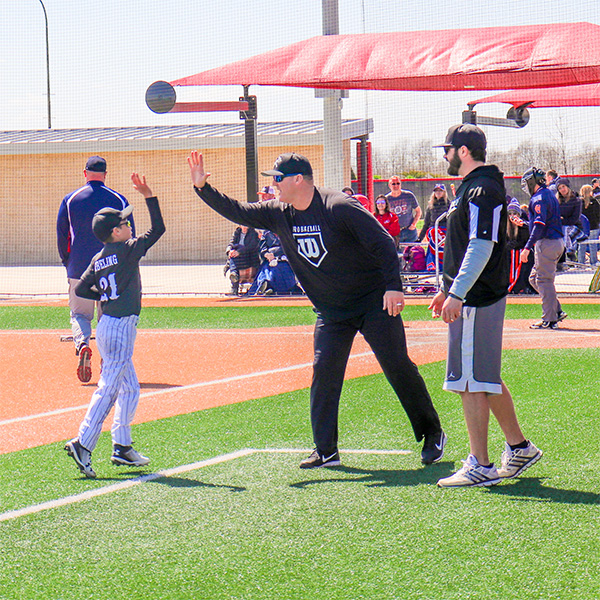 Baseball coach gives a high-five to a young ballplayer as a teammate looks on.