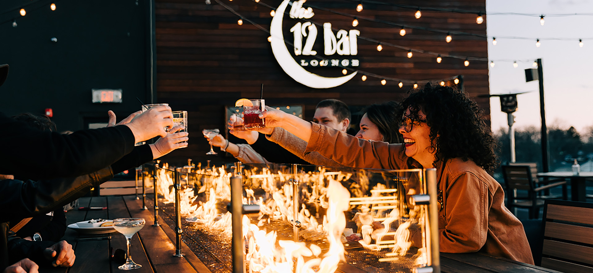 Friends toasting their drinks on the rooftop at The 12 Bar Lounge in Peoria Heights